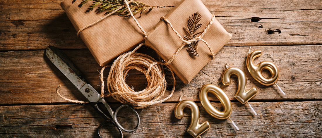 Prezenty zapakowane w beżowy papier. Poniżej złote świeczki w kształcie cyfr 2026