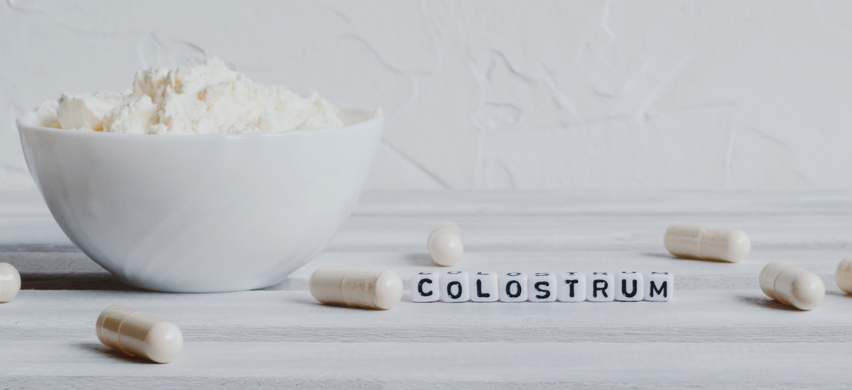 Kapsułki i proszek colostrum obok napisu „Colostrum” na jasnym tle