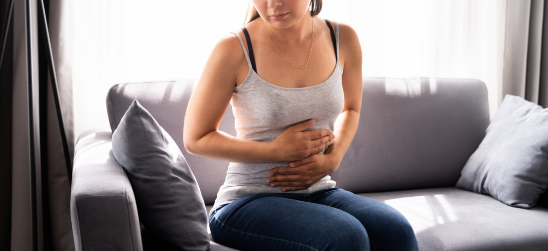 Młoda kobieta siedzi na kanapie trzymając się za brzuch ponieważ ma objawy pms (zespołu napięcia przedmiesiączkowego)