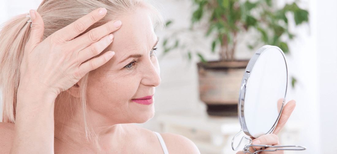 Uśmiechnięta kobieta o blond włosach ogląda swoją lśniącą cerę bez zmarszczek oraz liczne baby hair po suplementacji kolagenu Primabiotic