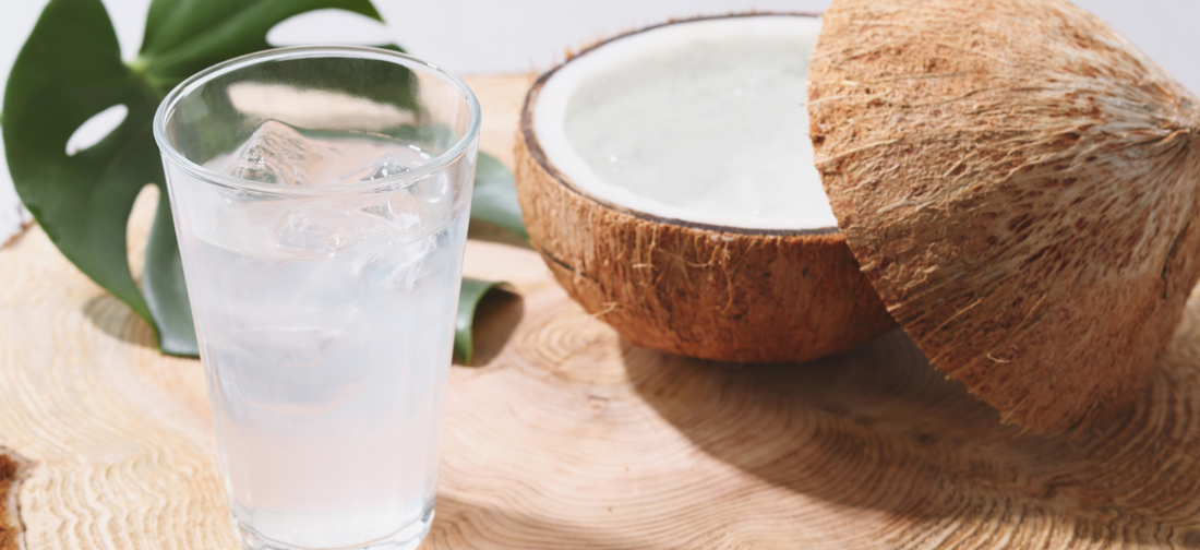 Szklanka wody kokosowej z kostkami lodu obok rozłupanego kokosa, naturalne źródło elektrolitów wykorzystywane w suplementach Primabiotic