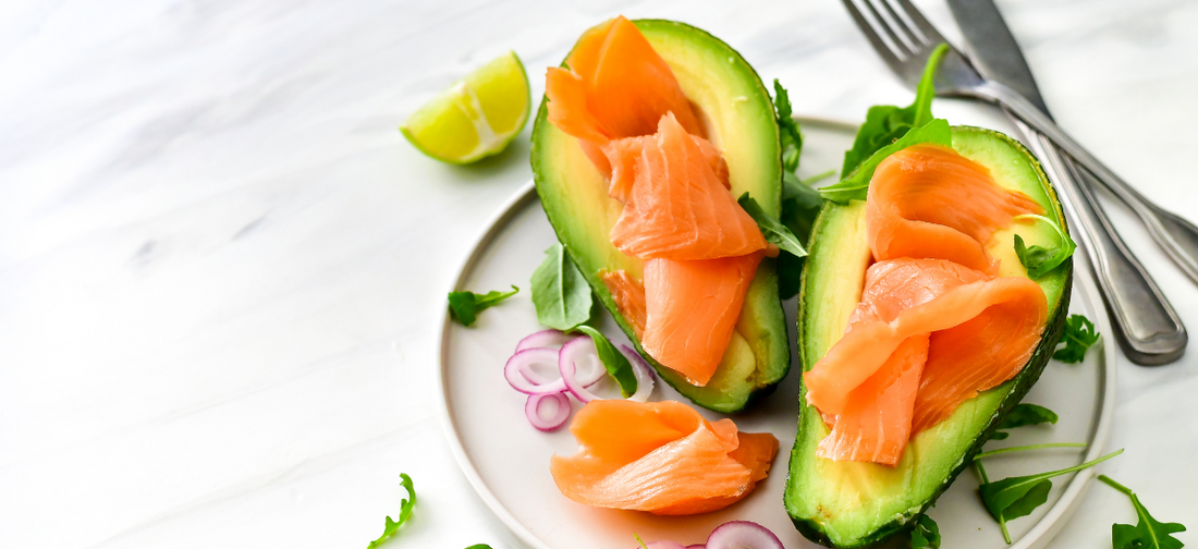 Awokado, łosoś i cebula ułożone na stole obok sztućców jako przykład produktów na wzmocnienie odporności