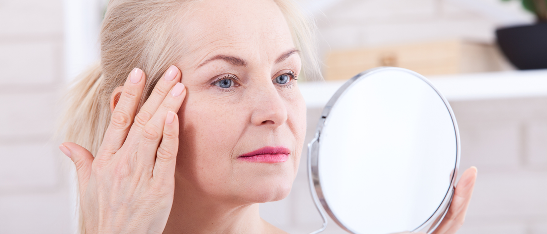 Starsza kobieta przegląda zmarszczki na swojej twarzy w lustrze