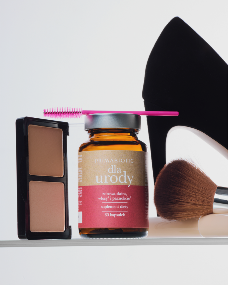 Suplement diety na włosy, skórę i paznokcie od Primabiotic w otoczeniu kosmetyków i butów na obcasie.