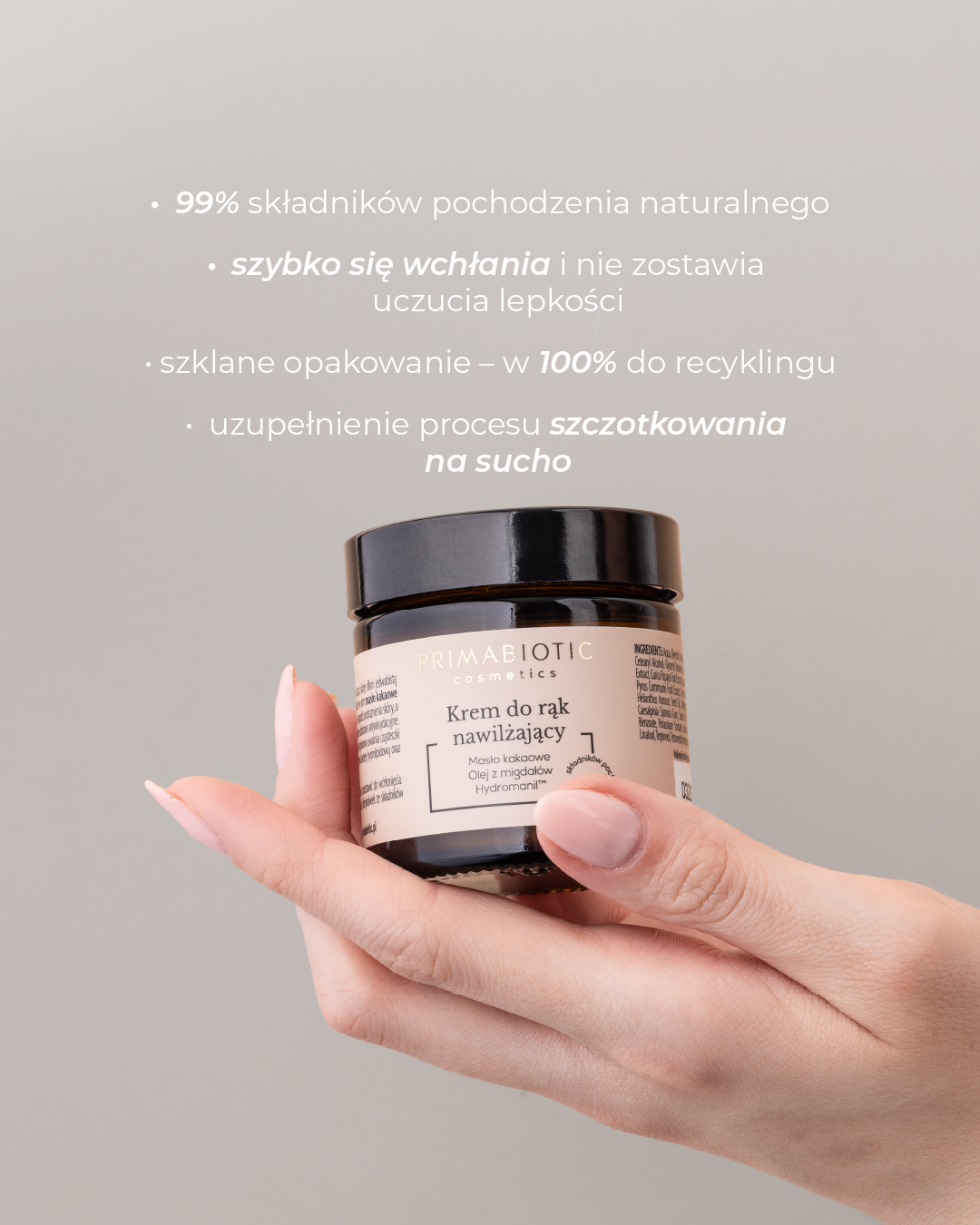 Krem do rąk nawilżający Primabiotic trzymany w zadbanej dłoni. Napis: 99% składników pochodzenia naturalnego, szybko się wchłania i nie zostawia uczucia lepkości, szklane opakowanie, uzupełnienie procesu szczotkowania na sucho