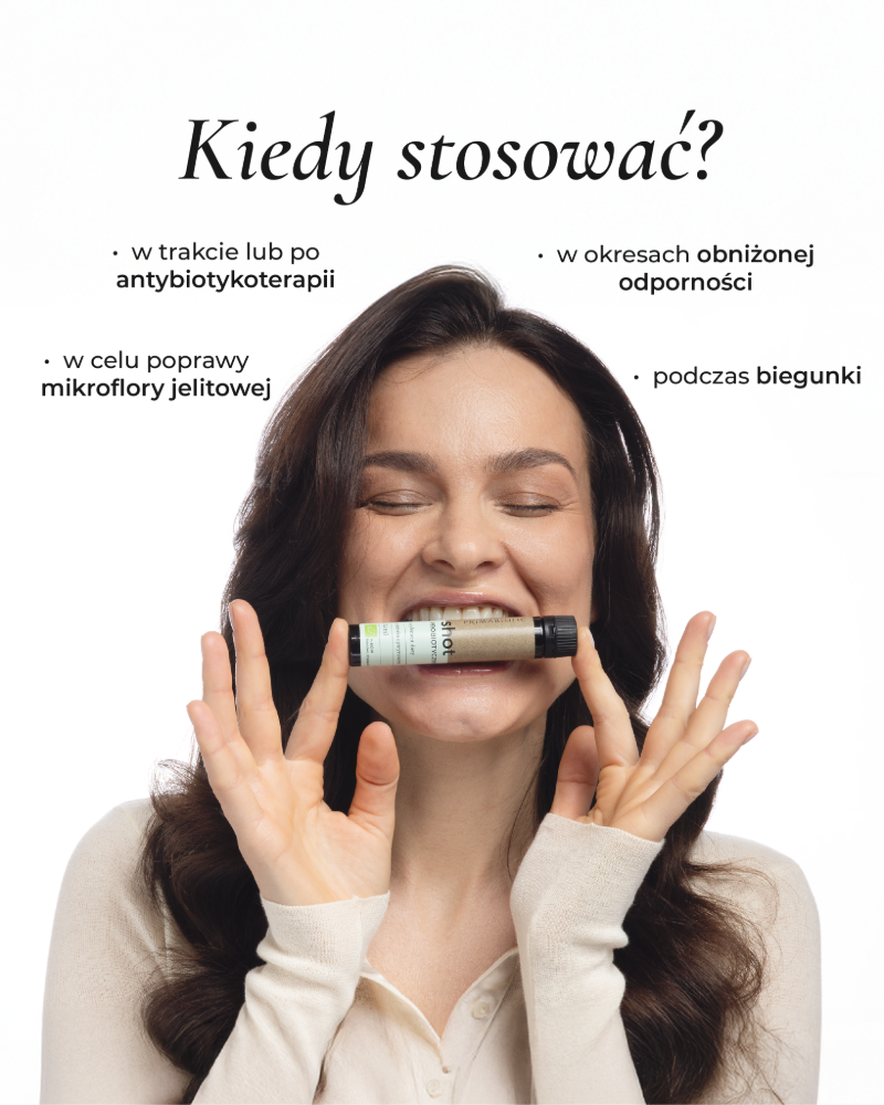 Kobieta o brązowych włosach trzyma w ustach shot probiotyczny Primabiotic jako wsparcie mikroflory jelitowej i odporności