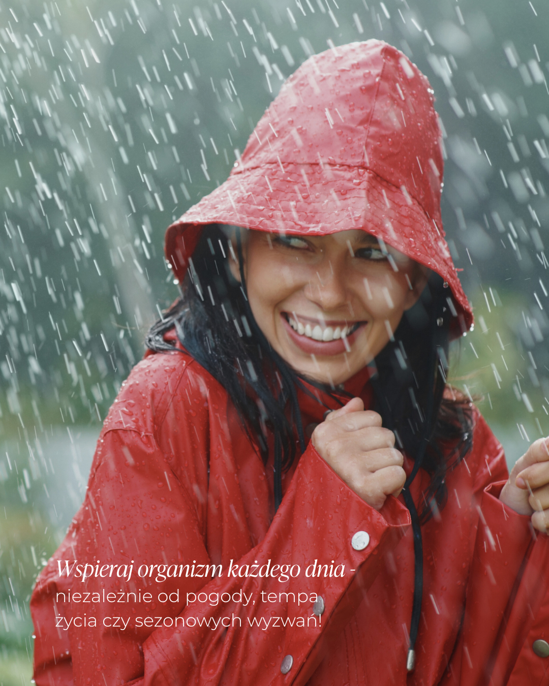 Kobieta w czerwonym płaszczu przeciwdeszczowym uśmiecha się w deszczu. Napis: wspieraj organizm każdego dnia - niezależnie od pogody, tempa życia czy sezonowych wyzwań!